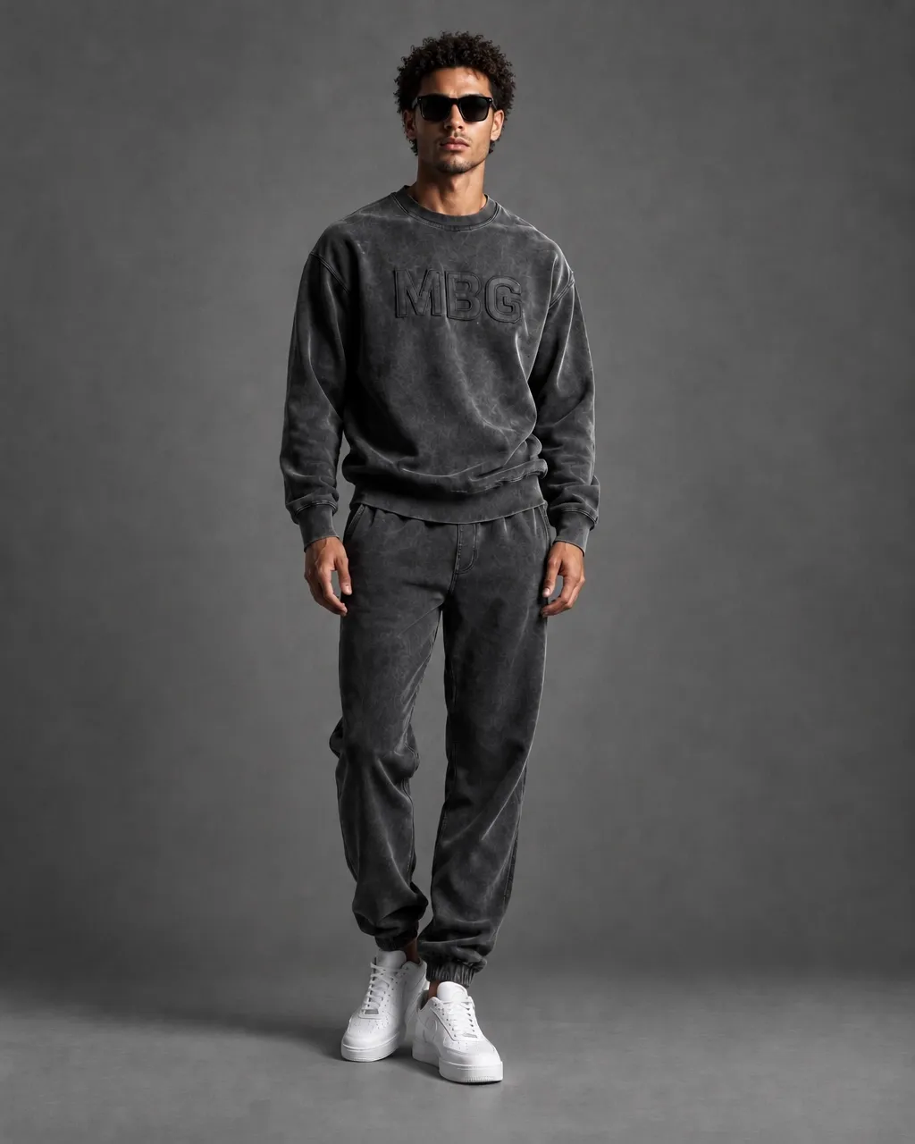Man wearing a charcoal MBG sweatshirt and joggers in a grey studio
