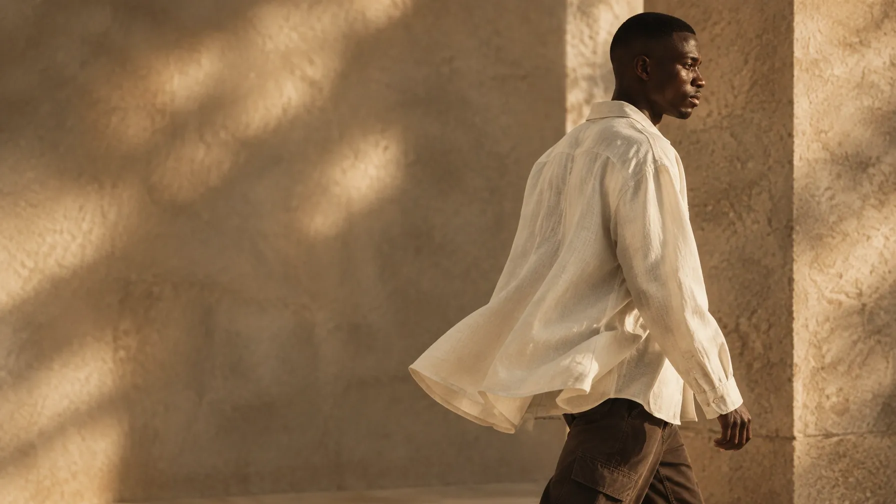 Person in a bone overshirt walking through a warm stone space
